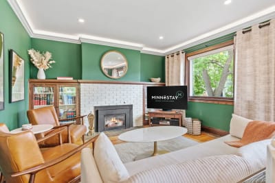 Cozy living room featuring green walls, leather chairs, and a white-brick fireplace.