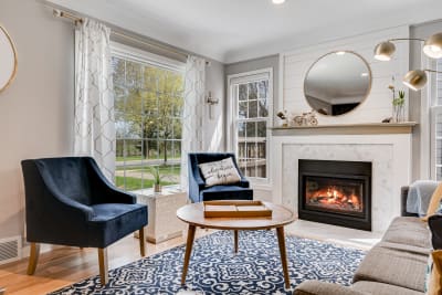 Cozy living room featuring navy blue armchairs, a fireplace, and large windows.