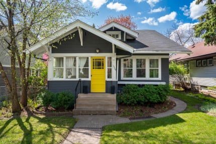Single-story house with gray siding and a yellow front door surrounded by greenery.