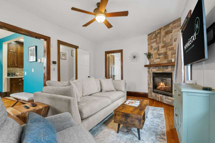 A living room featuring a light gray sofa, a rustic wooden coffee table, and a stone fireplace.