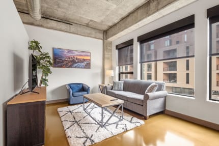 Modern living room featuring a gray sofa, blue accent chair, and large windows, illuminated by natural light.