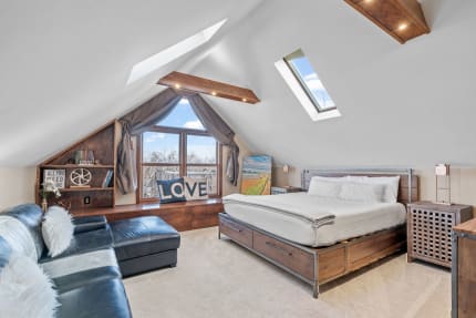 Cozy attic bedroom featuring a wooden bed, black leather sofa, and large windows.