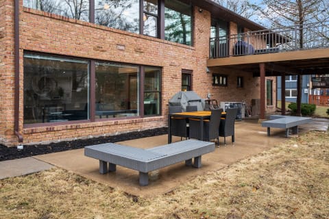 Cozy outdoor patio with dining table, chairs, and grill behind a brick house.