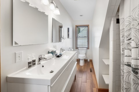 A modern bathroom featuring a double vanity, wooden flooring, and natural light from a window.