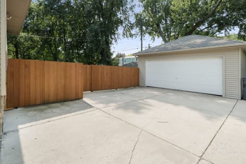 Spacious driveway with wooden fence and white garage in a suburban setting.