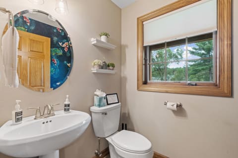 Modern bathroom featuring a circular mirror, stylish sink, and a window with greenery outside.