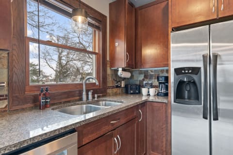 A well-appointed kitchen featuring wooden cabinets, granite countertops, and a view of trees through the window.