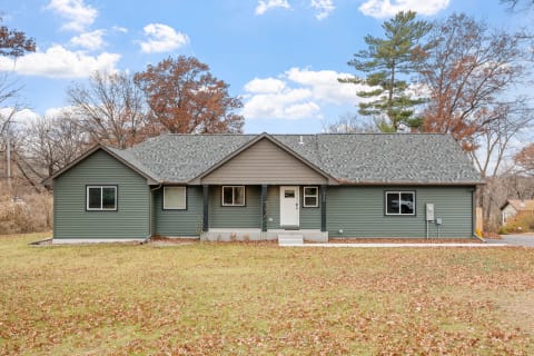 Single-story house with green siding and grey roof in a yard filled with leaves.
