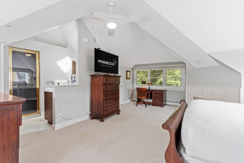 Spacious attic bedroom with a wooden sleigh bed and a workspace, featuring a TV and a shower.