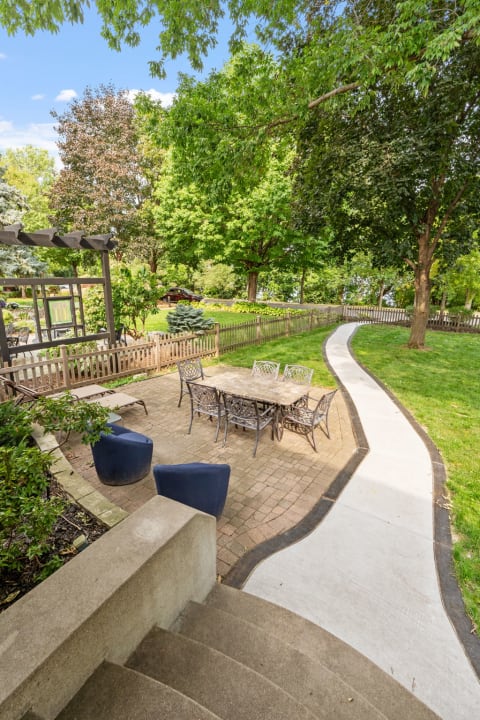A garden patio with a dining table surrounded by chairs, a winding pathway, and lush trees.