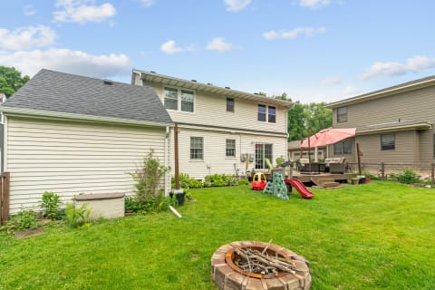 Suburban backyard with lawn, fire pit, children's toys, and seating area beneath an umbrella.