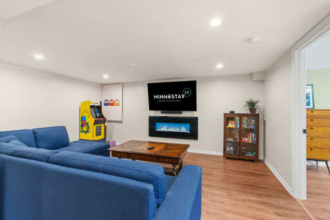 Modern living room with blue sofa, arcade game, and electric fireplace.