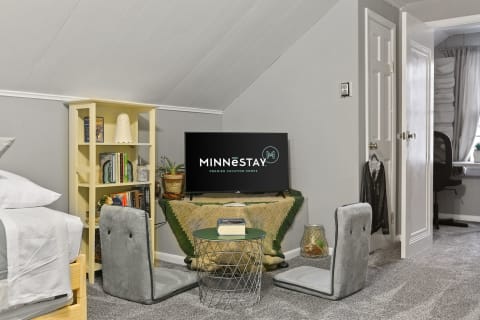 A cozy attic space with a bed, TV, bookshelf, and floor chairs