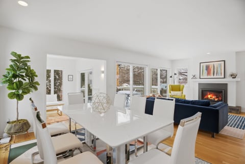 A modern dining room with a white table, cozy fireplace, and colorful decor.