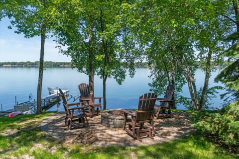 Lakeside scenery with a fire pit and Adirondack chairs in a natural setting.