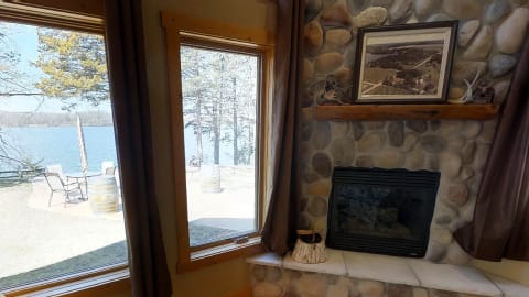 Interior of a room with a stone fireplace and a view of a lake through large windows.