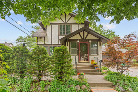 Traditional two-story home with a red door, surrounded by flower pots and greenery.