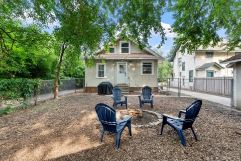 Outdoor scene of a backyard with a fire pit, Adirondack chairs, and a house.