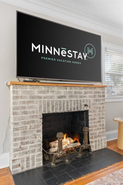 Living room with a flat-screen TV showing MINNESTAY logo above a fireplace with a flickering fire.