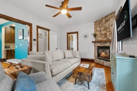 A living room featuring a light gray sofa, a rustic wooden coffee table, and a stone fireplace.