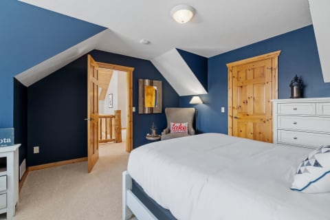 A bedroom with navy blue walls, a white bed, and wooden accents.
