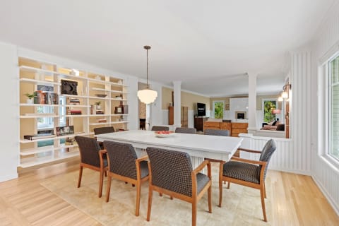 Modern dining area featuring a white table, woven chairs, and an organized bookshelf.