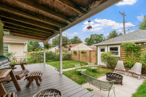View of a backyard with a covered patio, green chairs, and a fire pit.