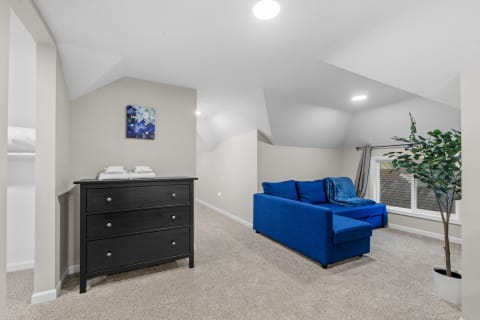 Attic space with a blue sectional sofa, black dresser, and artwork on the wall.