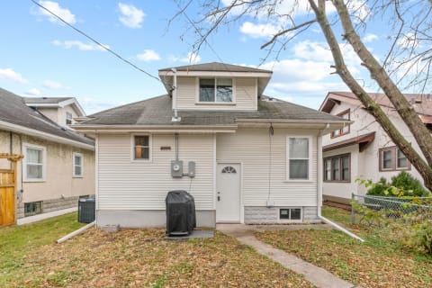 Exterior view of a two-story house with light siding, a porch, and a grill in the yard.