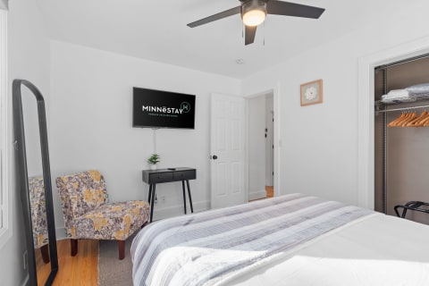 Interior view of a cozy bedroom featuring a comfortable bed, floral chair, and mounted television.