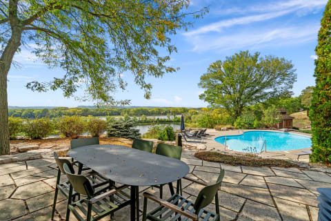 Outdoor dining area overlooking a pool and calm water surrounded by greenery.