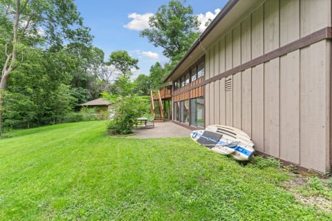 Backyard scene with a two-story house, large windows, and paddleboards on the grass.