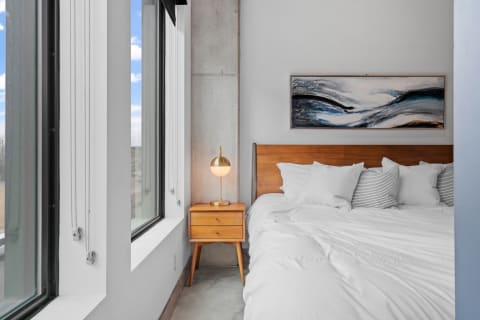 Modern bedroom featuring a bed with white linens, a wooden nightstand, and abstract artwork on the wall.