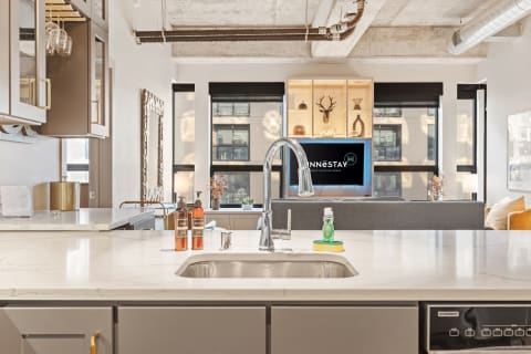 Modern kitchen with marble counter, stylish bottles, and a view of the living area.