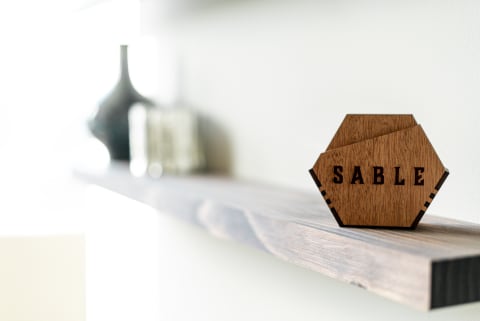 Wooden decor item with the word 'SABLE' on a shelf, with blurred decorative items in the background.