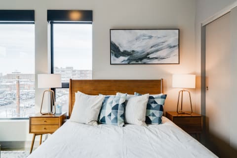 A modern bedroom with a light wood bed, geometric pillows, and a view of snow outside the window.