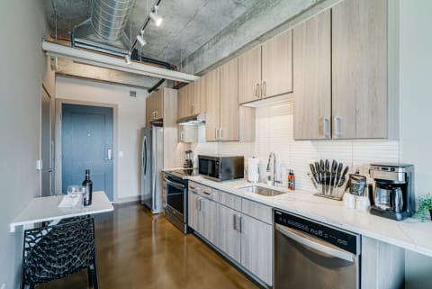 Modern kitchen with light wooden cabinets, stainless steel appliances, and polished concrete flooring.