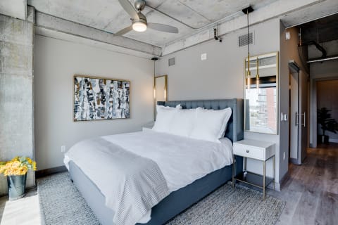 Modern bedroom featuring an upholstered bed, abstract artwork, and industrial elements.