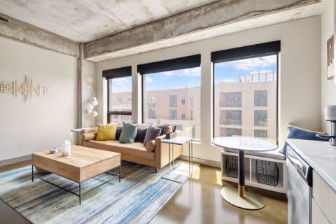 A stylish industrial living room featuring a leather sofa, wooden coffee table, and large windows.