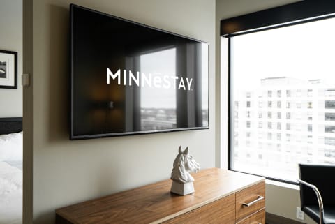 Modern hotel room with 'MINNēSTAY' logo on TV and a horse head sculpture on the dresser.