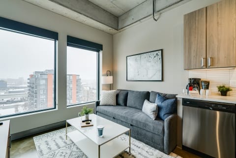 A stylish living room with a gray sofa, white coffee table, and city view through large windows.