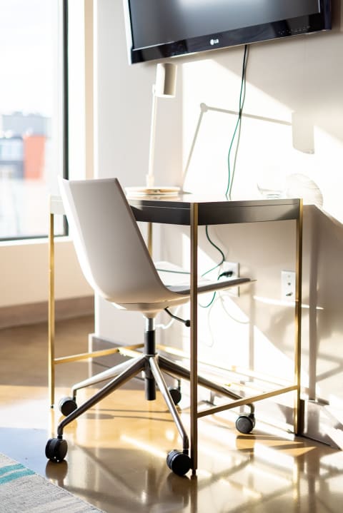A minimalist desk with a black surface and gold legs, paired with a white office chair, and a nearby TV.