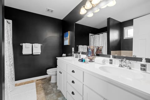 A modern bathroom featuring black walls and white fixtures with two sinks and a decorative shower curtain.