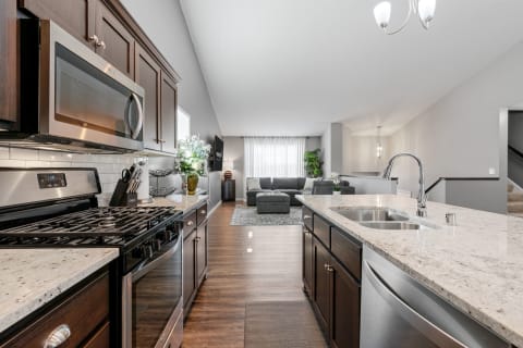 An open-concept kitchen and living area with dark cabinets, stainless appliances, and a cozy living space.