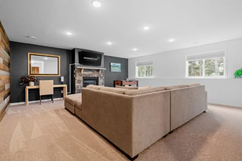 A cozy living room featuring a sectional sofa, desk, fireplace, and large windows.