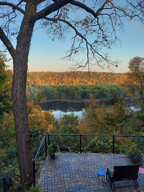 A scenic view featuring autumn foliage and a serene river from a stone patio.