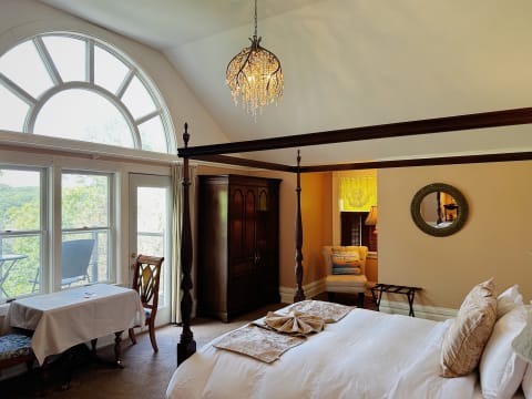 Cozy bedroom with a four-poster bed, large arched window, and warm decor details.