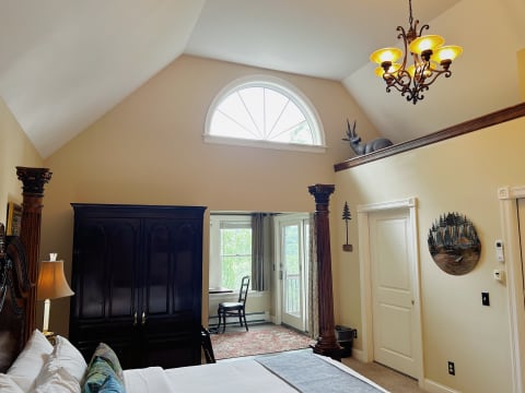 An elegant bedroom with vaulted ceilings, chandelier, and a view of a balcony.