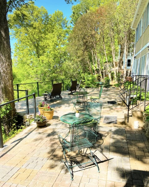 An inviting outdoor patio with green chairs and tables surrounded by trees and sunshine.
