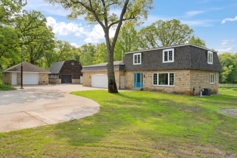 A residential property with a brick exterior, a blue door, and garages, set in a green landscape.